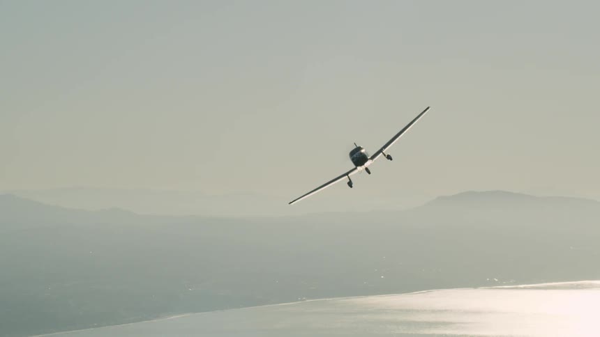 Airplane flies near hills over a large body of water on a sunny day
