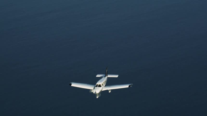 A small plane flies over the water