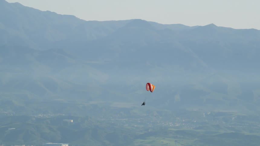 A person is paragliding over a community in a mountain basin in daylight