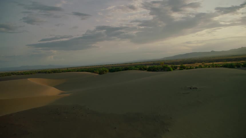 Sand dunes cover the landscape as clouds pass above