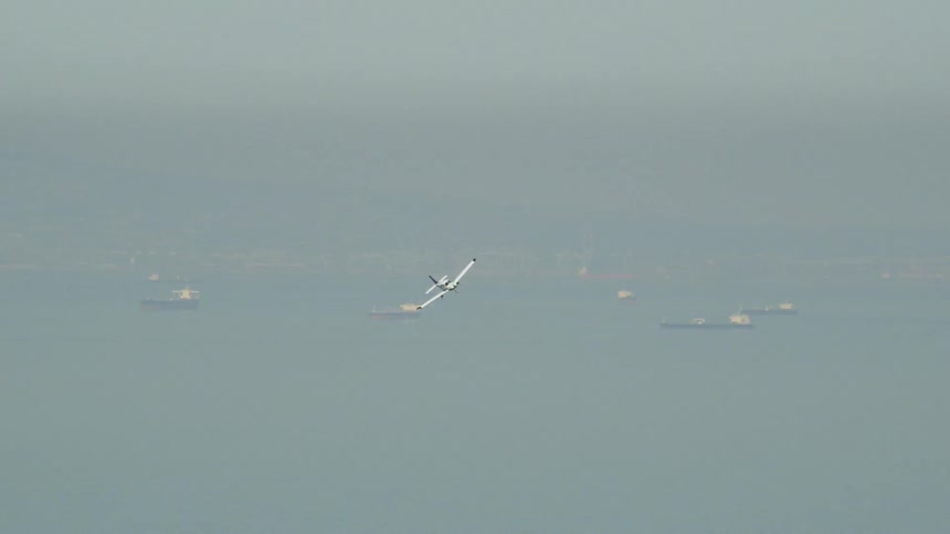 Small airplane flies over a large body of water with boats floating below
