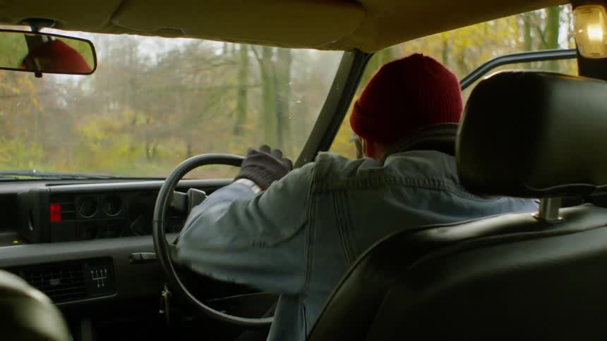 A man is getting out of a car in a wooded area on a cold day