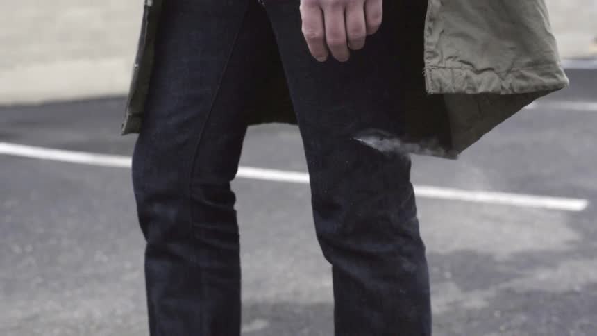 Close view of a man walking in a parking lot as white smoke streams out from a slit in his jeans