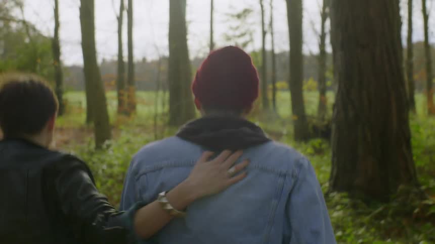 Woman pats a mans back as he smokes while they walk in the woods