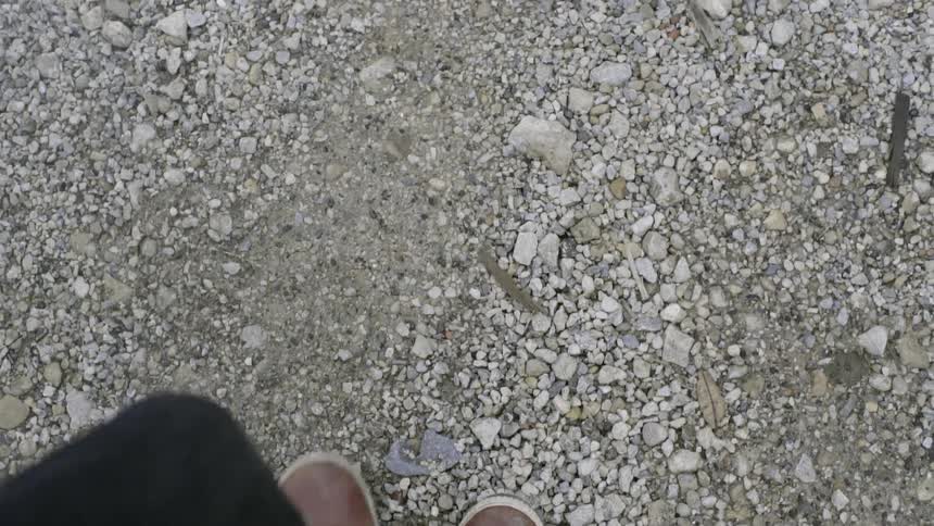 A view of a person's feet and shins as they walk over a rocky area and smoke billows from the cuff of their pants