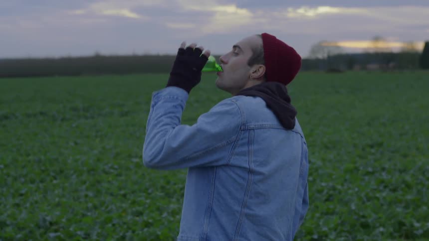 Man drinks from a bottle as he stands in a field