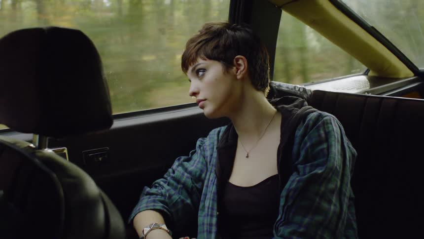 A woman is leaning back as she travels in a car in daylight