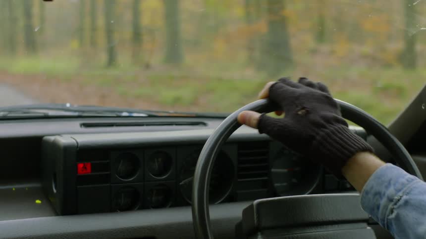A man wearing fingerless gloves drives a car