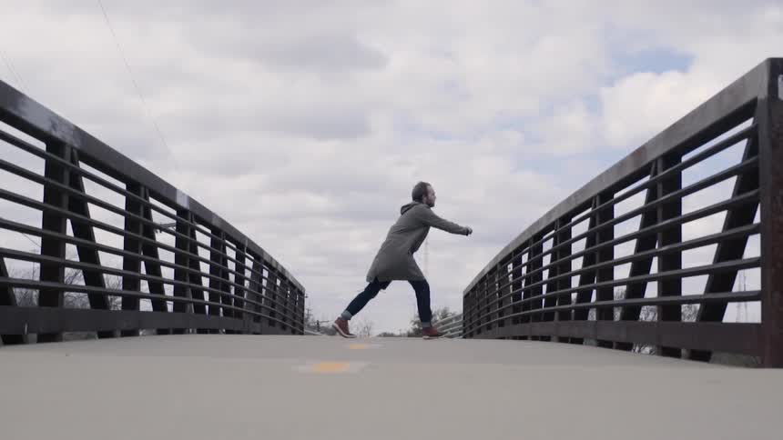 Man walking over a bridge bends over as if in pain then runs to lean over the barrier
