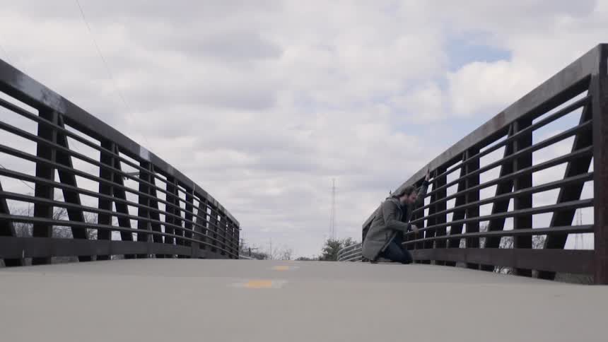 Man crouches down and looks out of the railing of a bridge