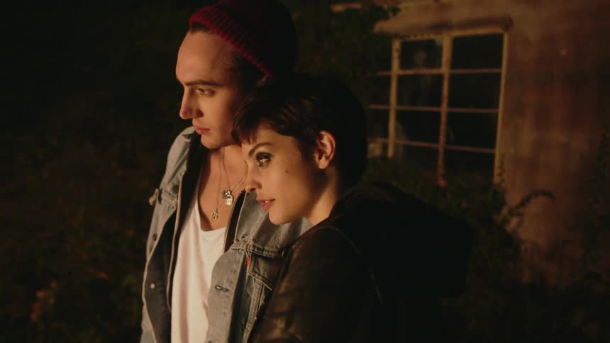 Man and woman stand outside a house at night looking at firelight