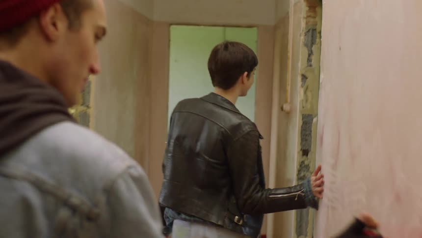 Man and woman walk down a hallway as the man spray paints the walls