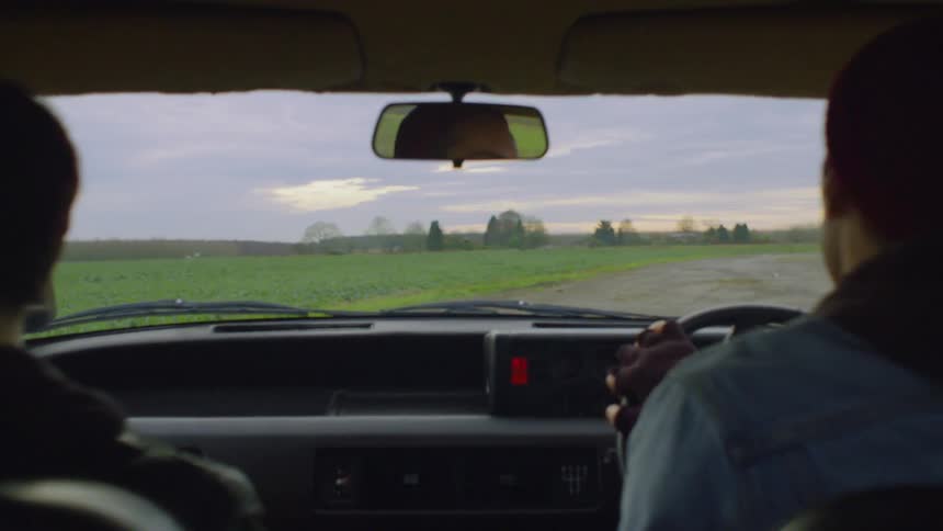 A man and woman drive on a rural road