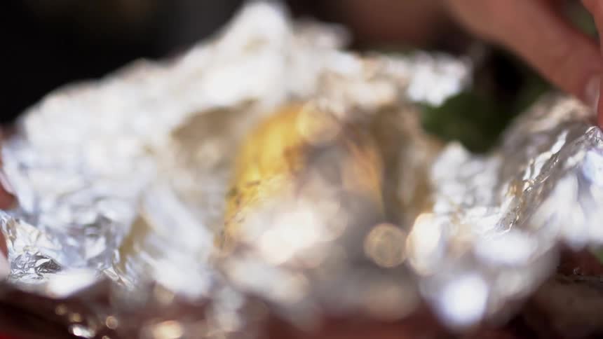 A grilled corn cob is unwrapped from foil