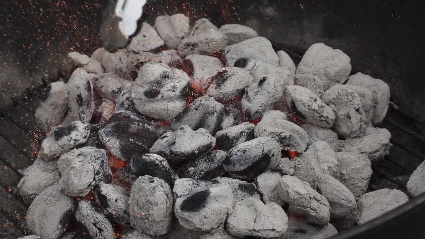 Tongs jostle white coals in a grill