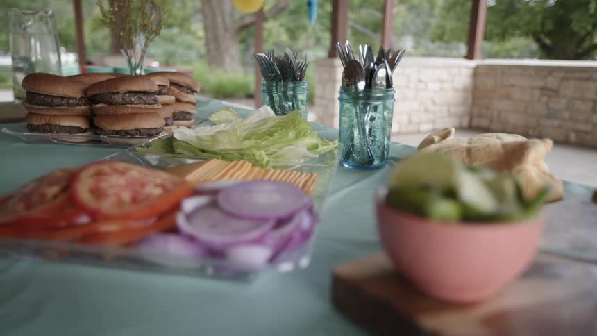 Long table with burgers and fixings set up outdoors buffet style