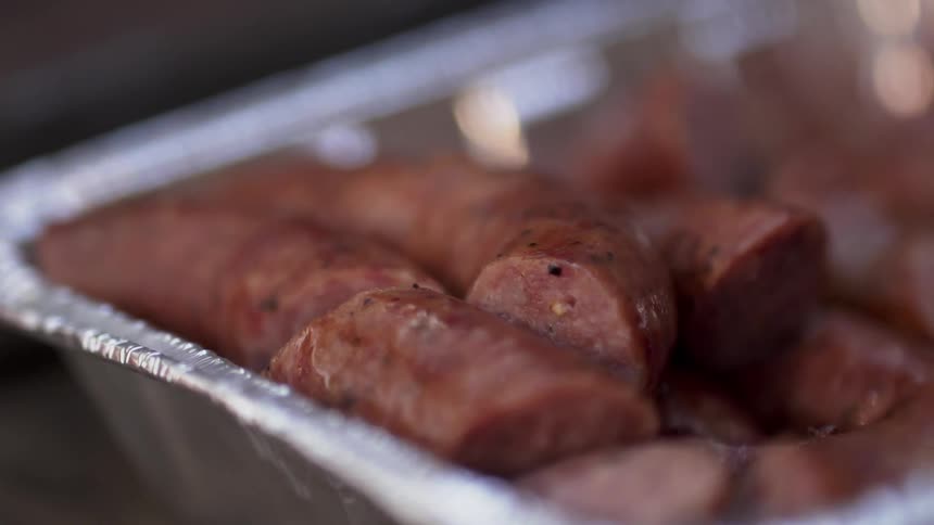 Grilled sausages sit in an aluminum foil pan