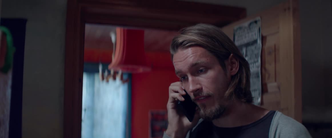 A focused male character listens intently while speaking on a cell phone inside.