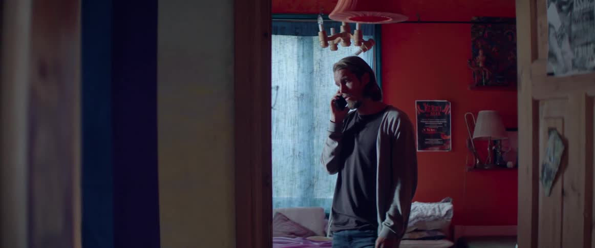 A man is standing in a hallway in his home having a conversation on a phone