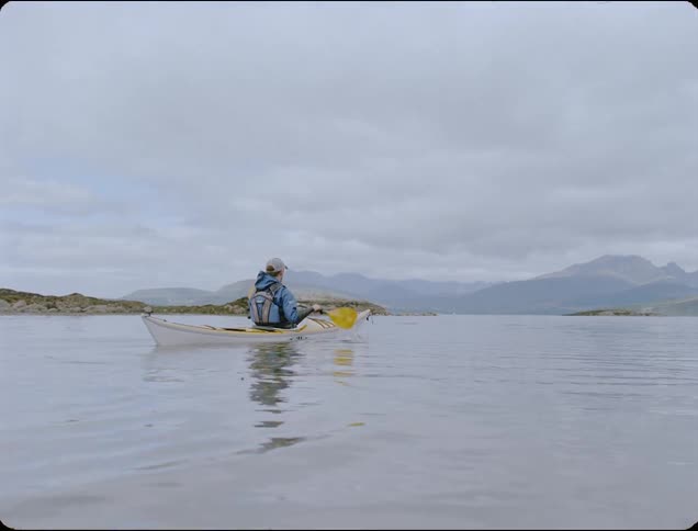 Man paddles a canoe through the lake near the mountains