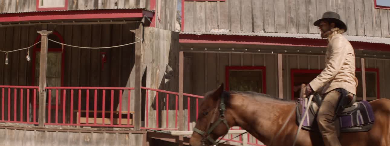 A man on a horse rides past old western buildings