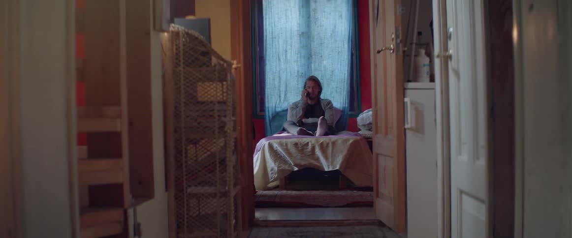 Distant view of a casual man sitting on a bed having phone call.