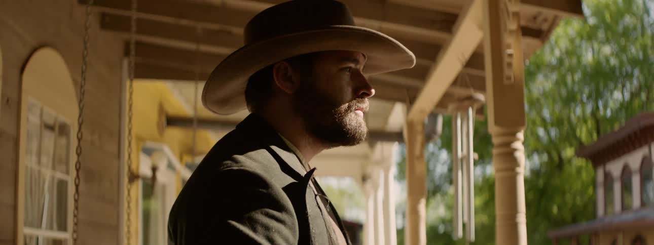 A man wearing a cowboy hat stands on a front porch