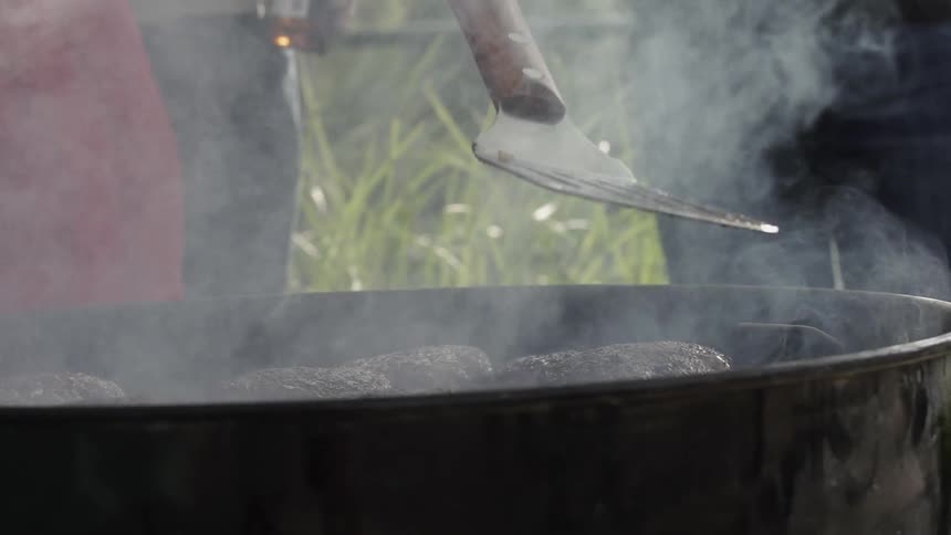 Hamburgers cooking on an open grill outside as two men stand near by with a burger flipper