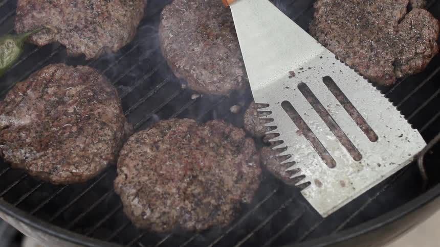 A spatula is pressed down on grilling burgers