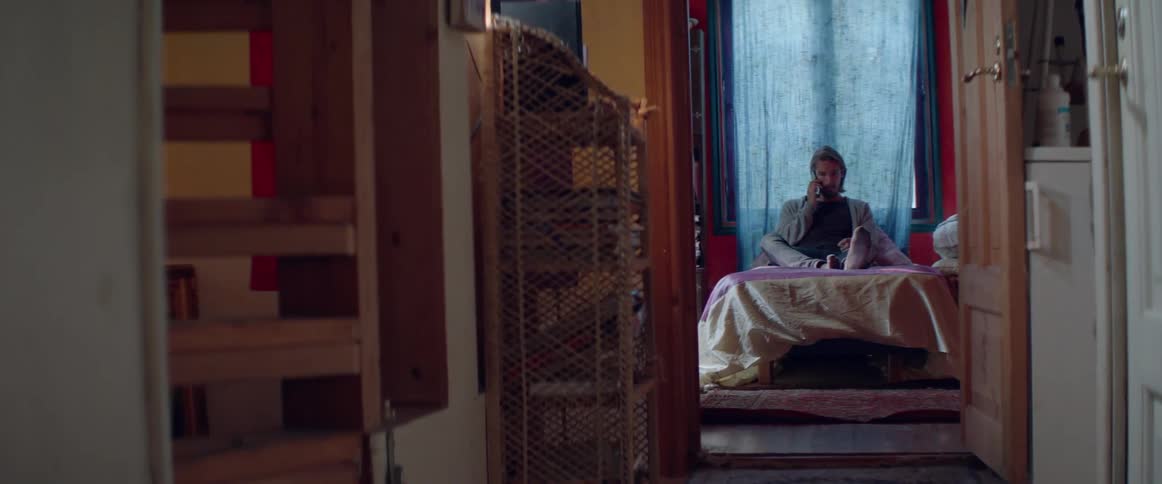 Distant view of a casual man sitting on his bed during phone call.