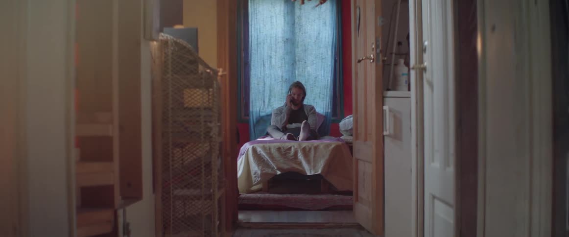 A casual bearded guy leans back against pillows during a phone call.