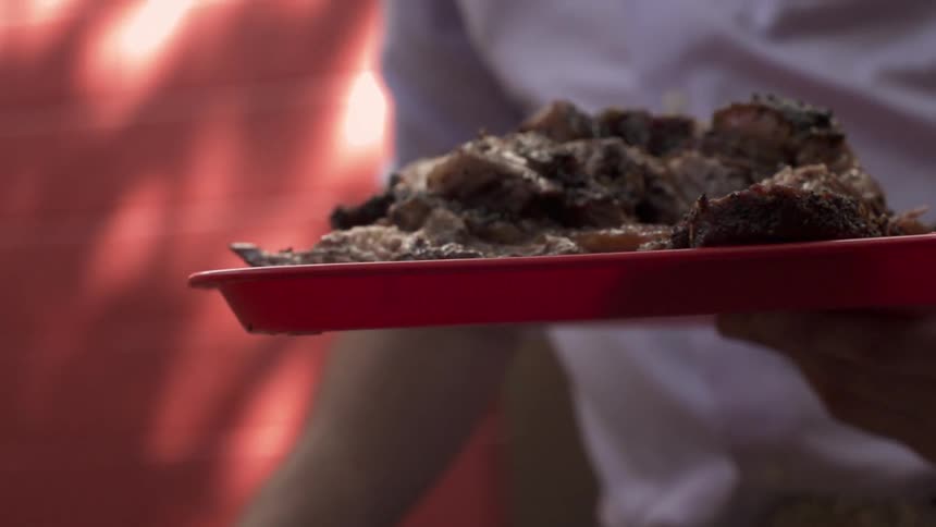 Man carrying a tray of sliced meat as he lays some tongs on a table