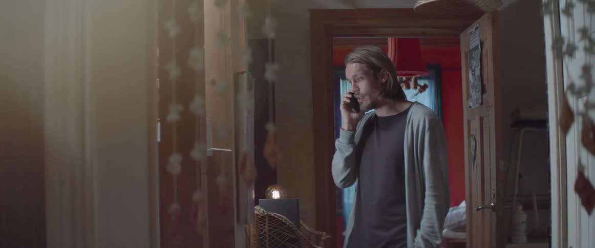A casual person paces near a wooden frame during a mobile phone conversation