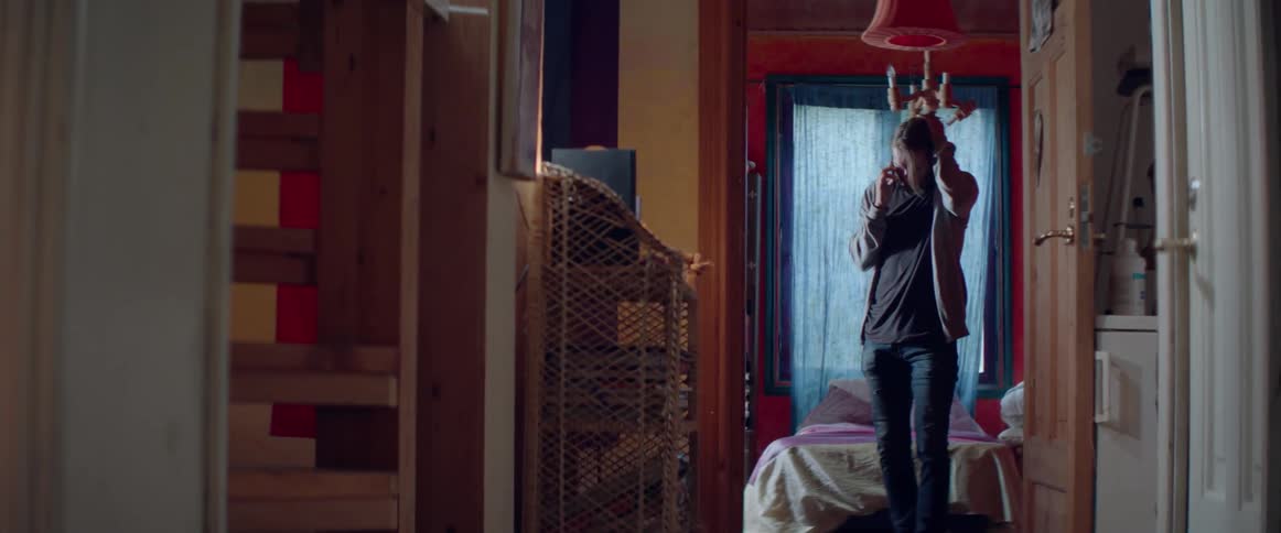 A young guy stands in his bedroom doorway while talking on the phone.