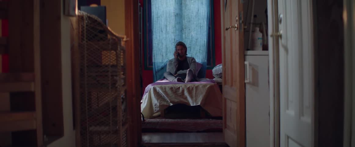 Distant view through an open doorway of a person sitting on bed.