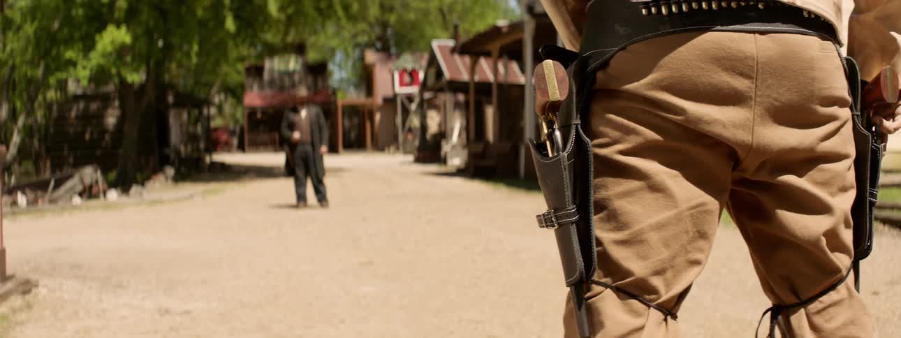 A man wearing a gun faces another in a duel standoff