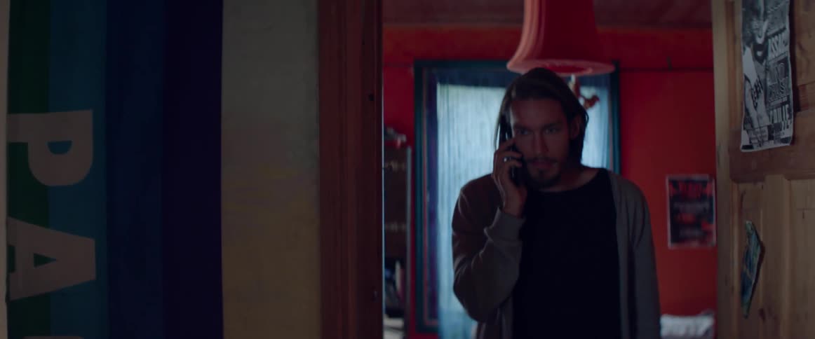 A serious male character has a focused phone conversation inside a colorful room.