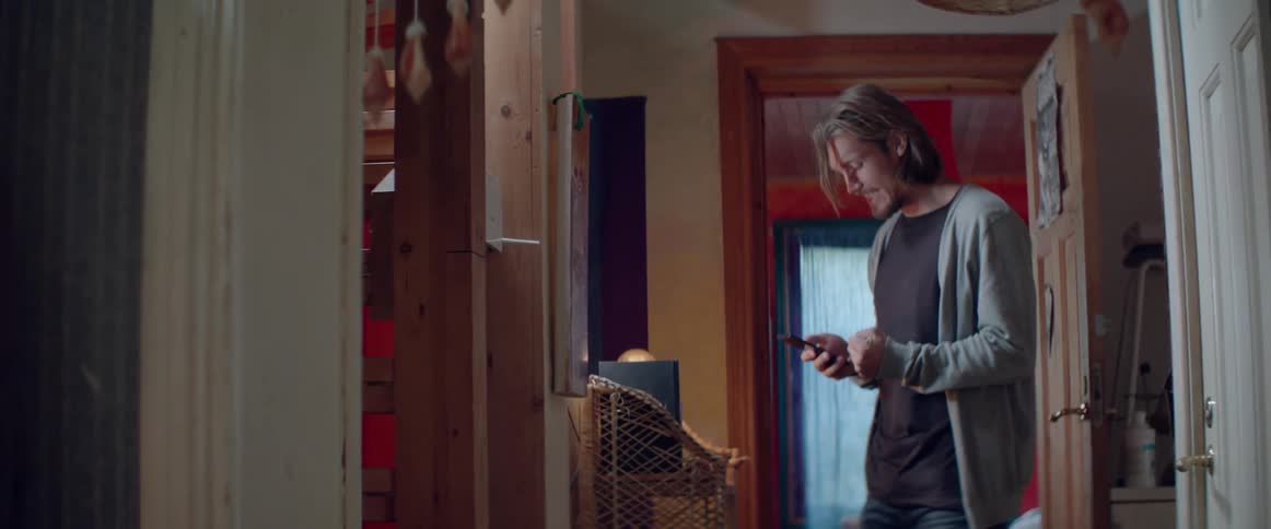 A worried man clenches his fist while checking his smartphone inside a hallway.