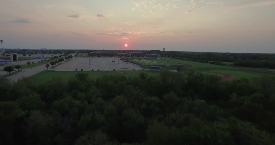 The sun sets over buildings and trees