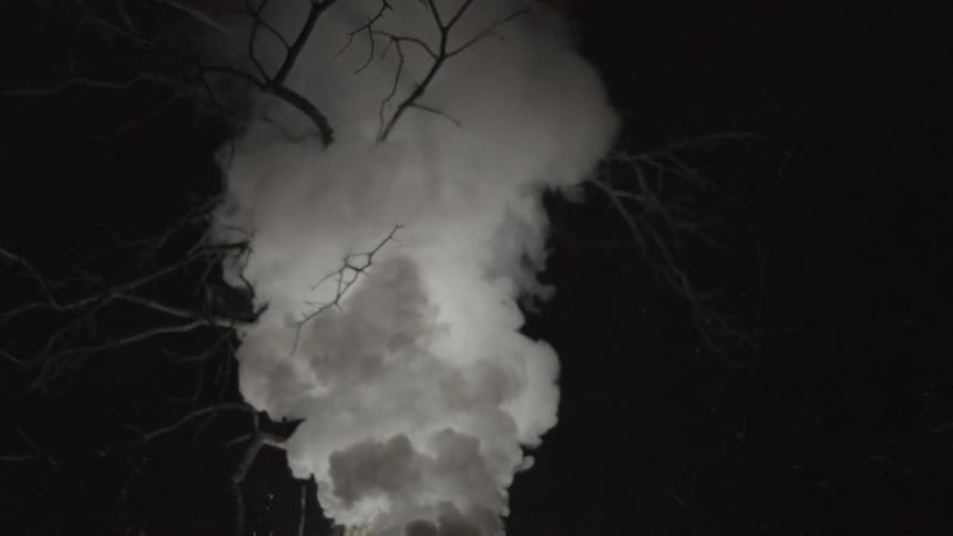 White smoke plumes toward the night sky