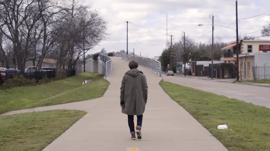 Man walking down a concrete walkway to a bridge on a cloudy day