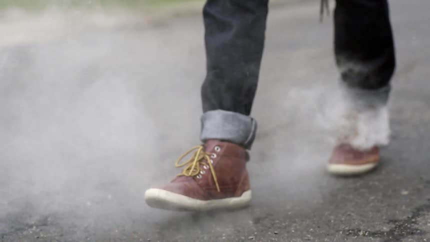 A man walking down a street as smoke rolls out from under his pant legs