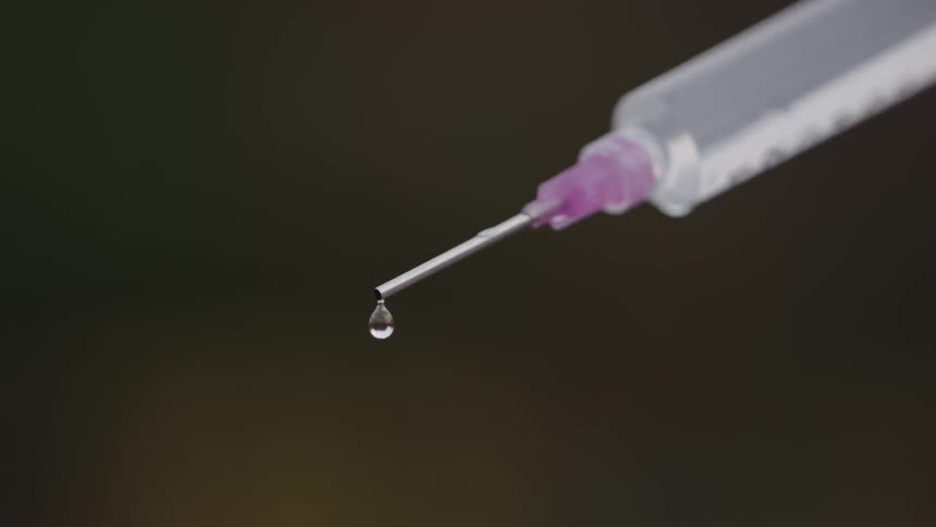 The needle drips a small drop of liquid