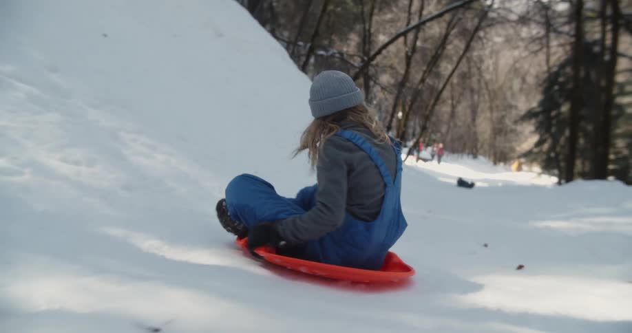 Child slides down a snowy hill on a small orange sled