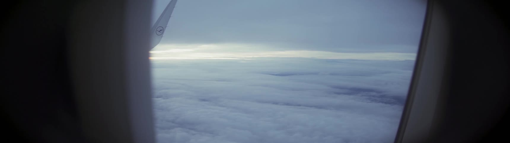 Light flashes on airplane wing as it flies over the white clouds
