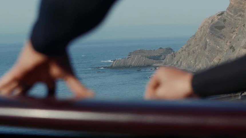 A surfer rubs wax on a surfboard