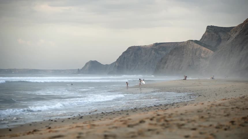 People wade into the ocean as a surfer carries his board out
