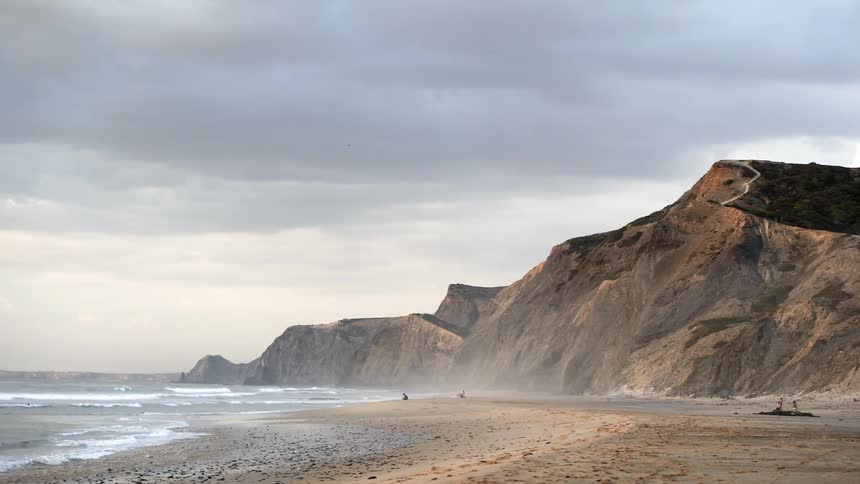 Waves roll in on a beach under a cloudy sky