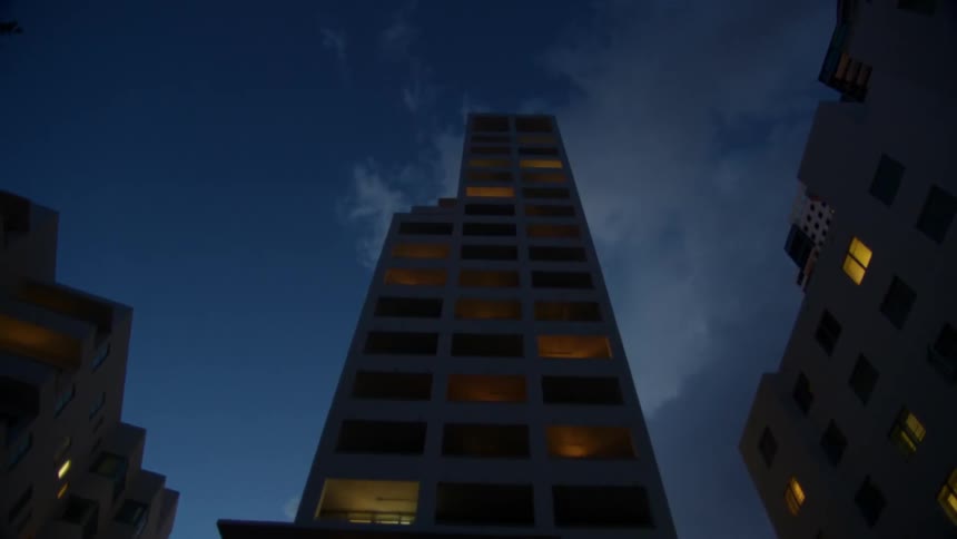 The tall building has only a few lit windows at dawn