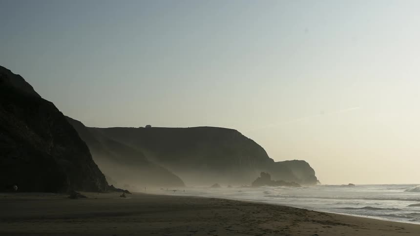 Waves crash into a sandy beach near the rocks